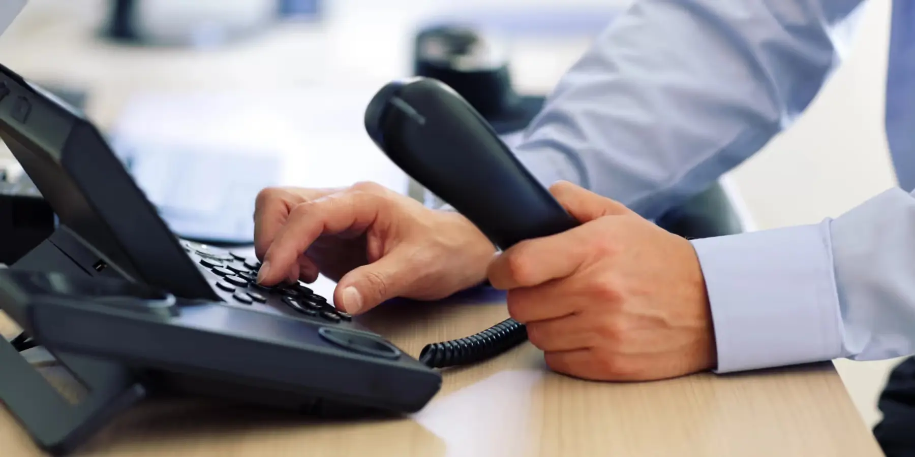 Person hält Telefonhörer und tippt Nummer auf einem Bürotelefon