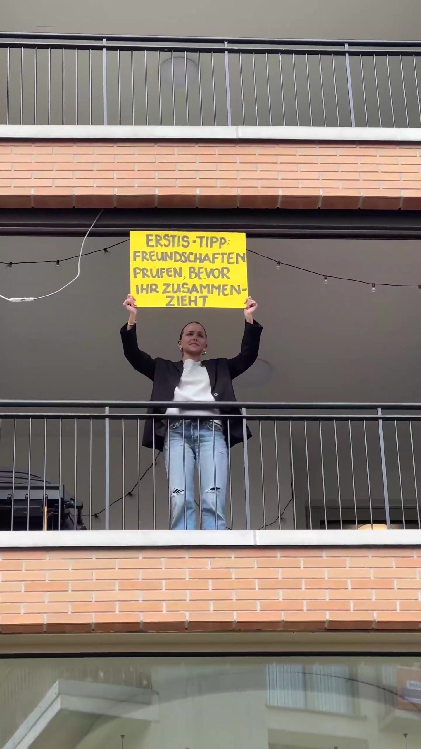 Eine Frau hält ein Schild auf dem Balkon ihrer Wohnung.
