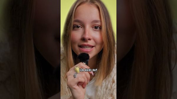 Eine junge Frau mit blonden Haaren hält ein Mikrofon und lächelt leicht; eingeblendeter Text „ich nicht da?“.
