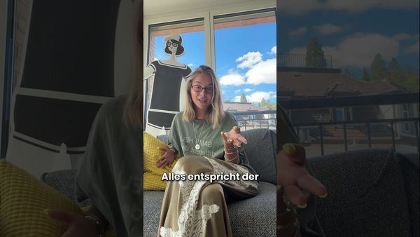 Eine Frau mit Brille sitzt auf einem Sofa und gestikuliert beim Sprechen, im Fenster hinter ihr ist eine Zeichentrickfigur eingeblendet; eingeblendeter Text „alles entspricht der“.
