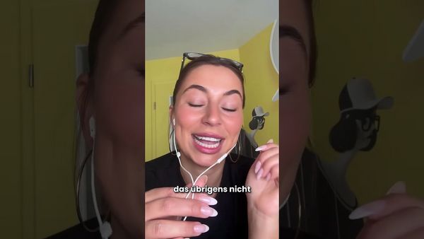 Eine Frau mit einer Brille auf dem Kopf lächelt, trägt Kopfhörer und hält einen in der Hand; eingeblendeter Text „das übrigens nicht“.