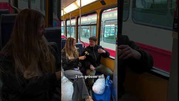 Zwei Personen sitzen sich im Zug gegenüber und unterhalten sich, im Bild eingeblendeter Text „2 cm grösser als“.