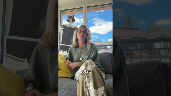 Eine Frau sitzt drinnen auf einem Sofa, hinter ihr ein grosses Fenster mit strahlend blauem Himmel; im Fensterrahmen steht eine Schaufensterpuppe mit Brille.