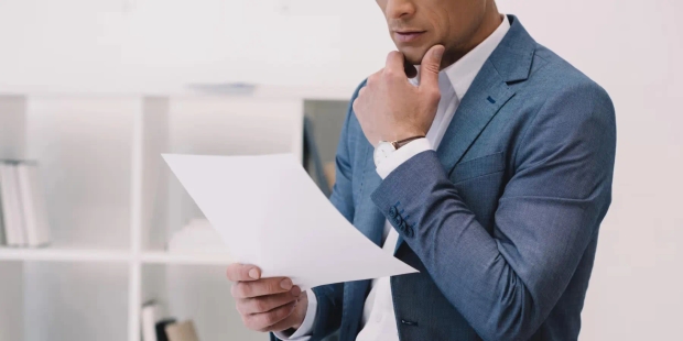 Homme en costume bleu lit pensivement un document