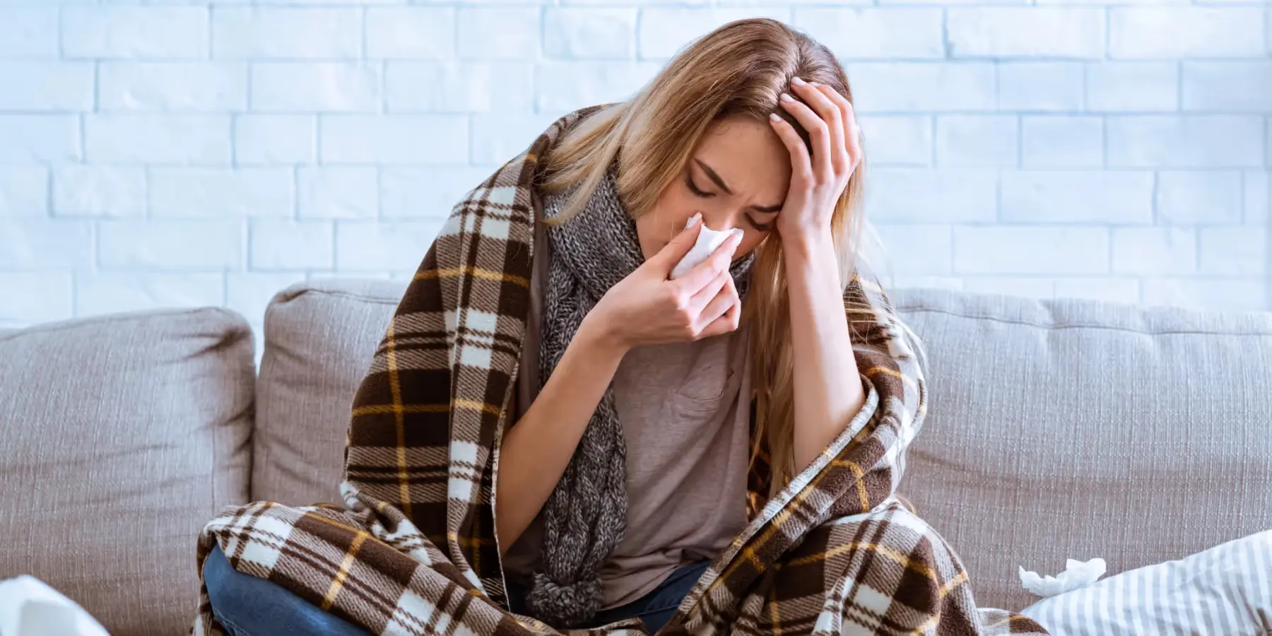 Kranke Frau in Decke gehüllt auf dem Sofa mit Taschentuch