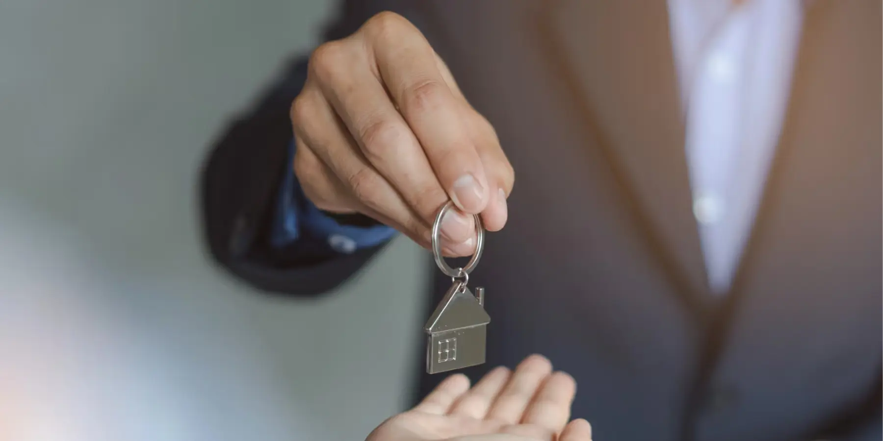 Personne en costume tend une clé avec porte-clé en forme de maison